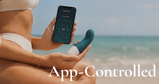 A person seated on a beach holds a smartphone displaying a control app screen while holding a teal and white personal massager